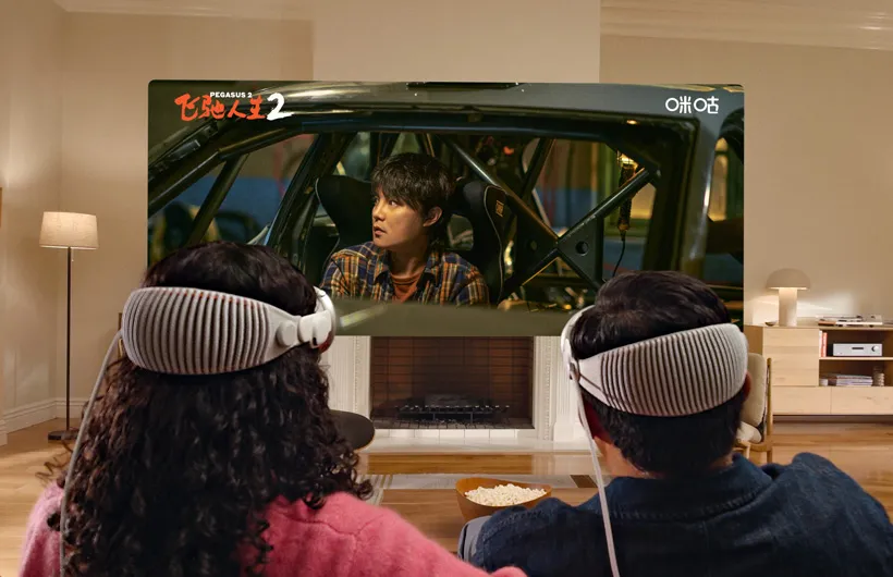 两个人头戴 Apple Vision Pro，并排坐在沙发上观看电影《飞驰人生 2》。