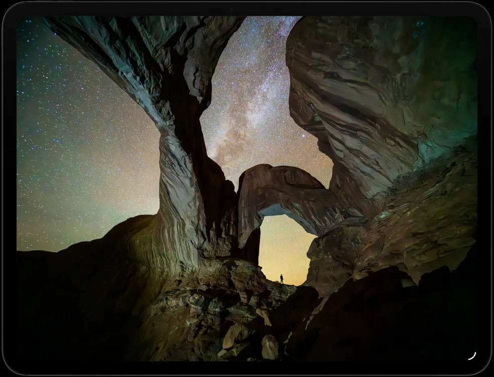 横屏放置的 iPad Pro，屏幕展示一张星空下的峡谷照片，峡谷中间站着一个人。