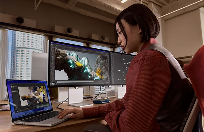 一个人在办公室环境中工作，MacBook Pro 连接着 Studio Display XDR。